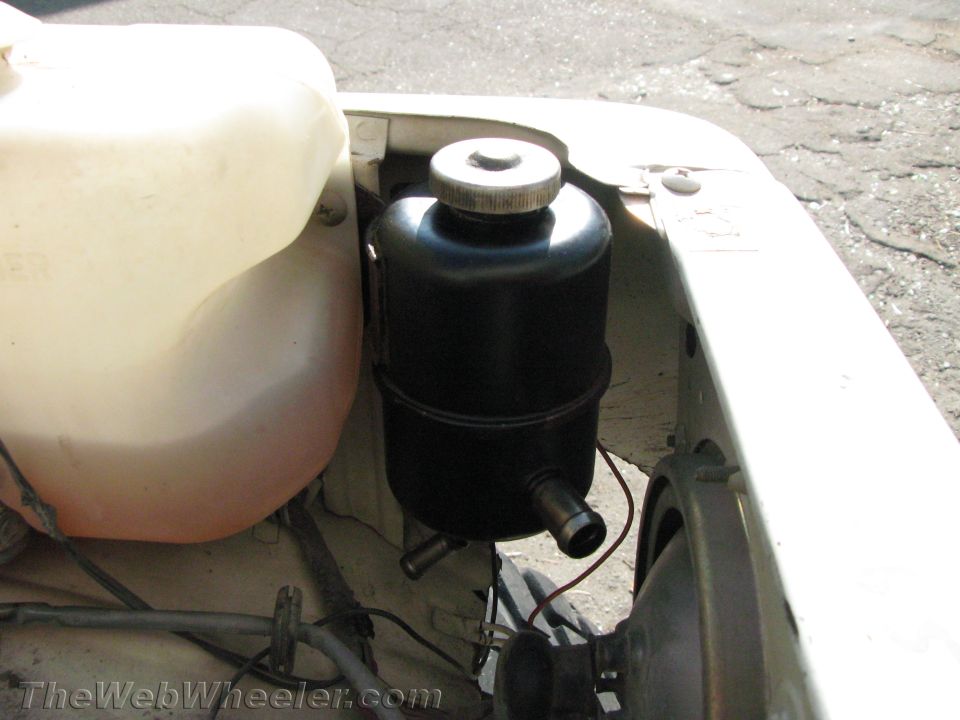 White vehicle engine bay with black power steering fluid reservoir and translucent fluid reservoir