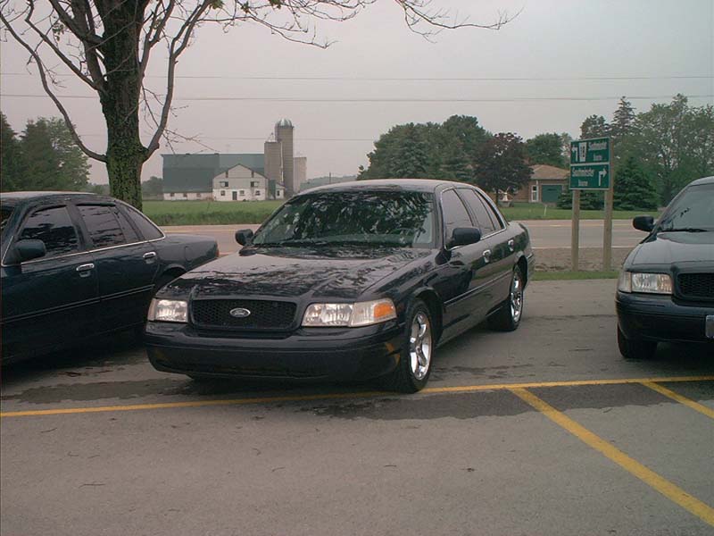 Black Ford Crown Victoria parked next to another car, front view