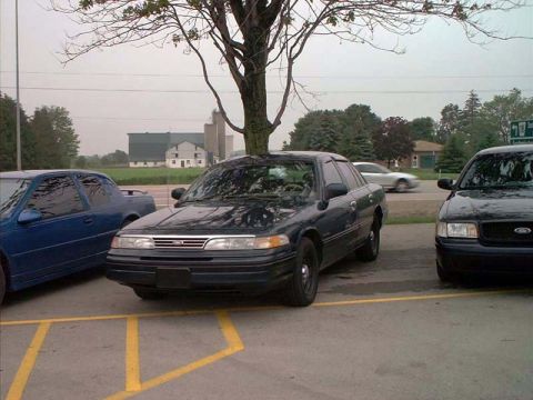 2000 Ford Crown Victoria - A black Ford Crown Victoria is parked next to a blue sedan and another black car.