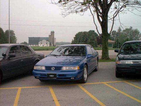 2000 Ford Crown Victoria - A blue coupe is parked in a lot next to other vehicles.