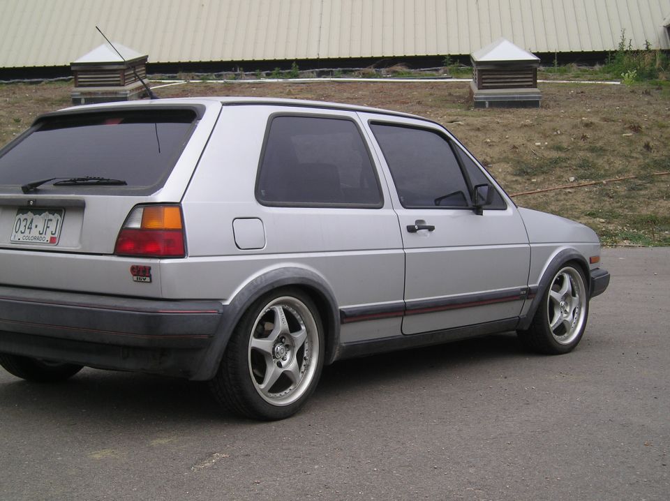 Silver hatchback with red stripe and GTI badge, rear 3/4 view