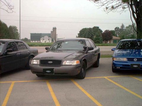 2000 Ford Crown Victoria - Two cars, a gray Ford Crown Victoria and a blue sedan, are parked in a lot.