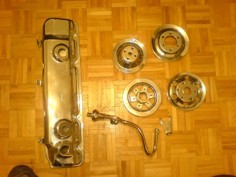 1985 Ford Bronco - Chrome valve cover and four hubcaps are laid out on a wooden floor.