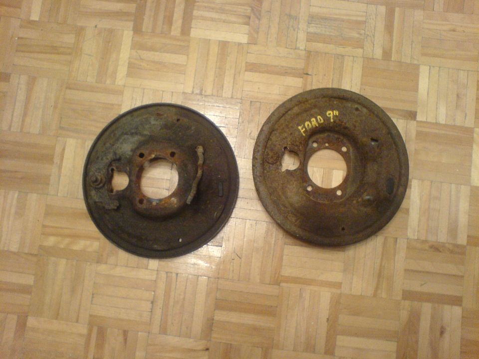 two rusty brake drums on a wood floor, one has 'FORD 9"' written on it