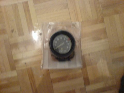 1985 Ford Bronco - A tachometer gauge is shown in its original packaging on a wooden floor.