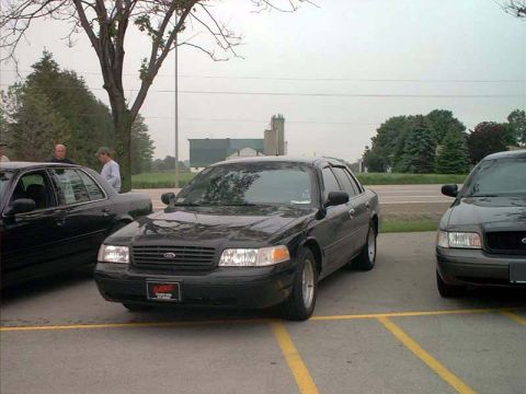 2000 Ford Crown Victoria - Two Ford Crown Victorias are parked side-by-side in a parking lot under an overcast sky.