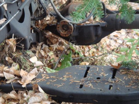 1996 Ford Bronco - The undercarriage of a vehicle, partially obscured by fallen leaves and evergreen branches, rests in an outdoor setting.