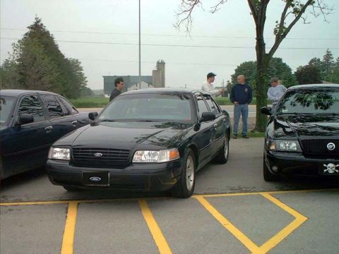 2000 Ford Crown Victoria - A black 2000 Ford Crown Victoria is parked in a lot next to another vehicle.