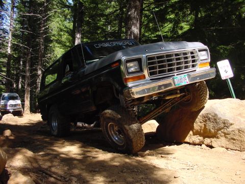 1979 Ford Bronco - A dark gray 1978 Ford Bronco navigates a challenging rocky off-road course with another vehicle visible in the background.