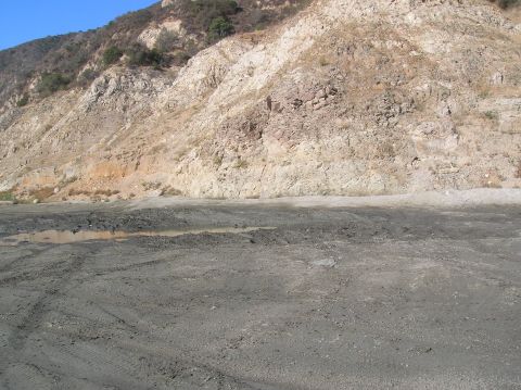 1985 Ford Bronco - A dirt road with tire tracks and a puddle is visible in front of a rocky hillside.