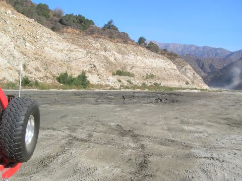 1985 Ford Bronco - A tire from a vehicle is visible in the foreground of a dry, mountainous landscape with tire tracks in the dirt.