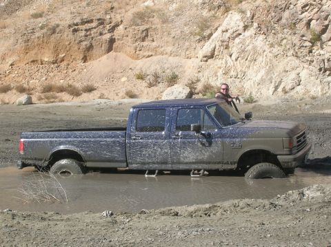 1985 Ford Bronco - A mud-splattered Ford F-350 crew cab truck is stuck in a muddy area with a person leaning on the driver's side window.