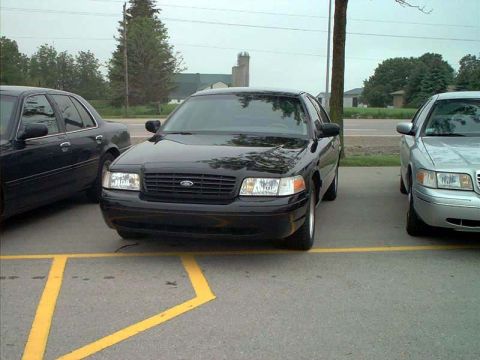 2000 Ford Crown Victoria - A black 2000 Ford Crown Victoria is parked in a lot, with another vehicle visible to its left and right.