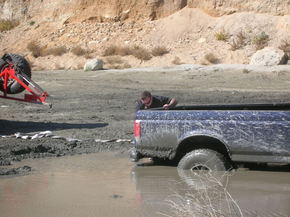Guy in a muddy blue pickup truck stuck in water, another vehicle with tires is nearby