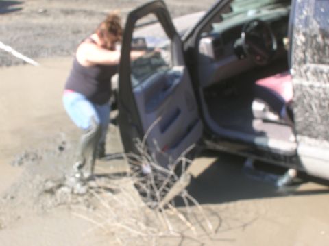 1985 Ford Bronco - A person exits a vehicle stuck in mud, with the driver's side door open.