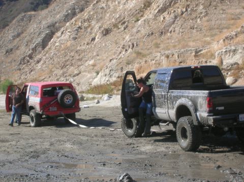 1985 Ford Bronco - Two off-road vehicles are stuck in the mud, with one being towed by the other.