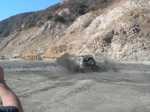 1985 Ford Bronco - An SUV navigates a muddy terrain, spraying dirt as it goes.
