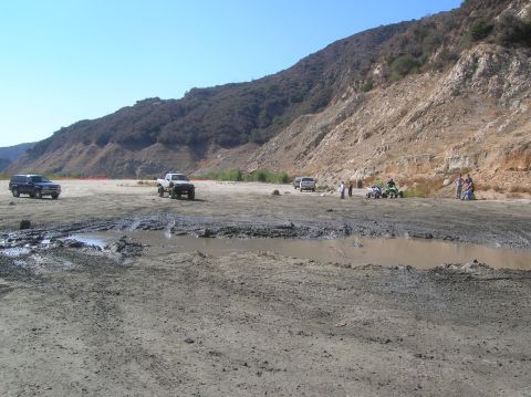 1985 Ford Bronco - A muddy landscape with several off-road vehicles and ATVs, suggesting an outdoor recreational area.
