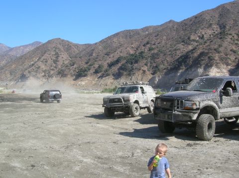 1985 Ford Bronco - Several off-road vehicles are parked in a dusty, mountainous area under a clear blue sky.
