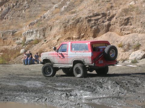 1985 Ford Bronco - A red and white Ford Bronco is covered in mud after off-roading in a rocky, dry landscape.