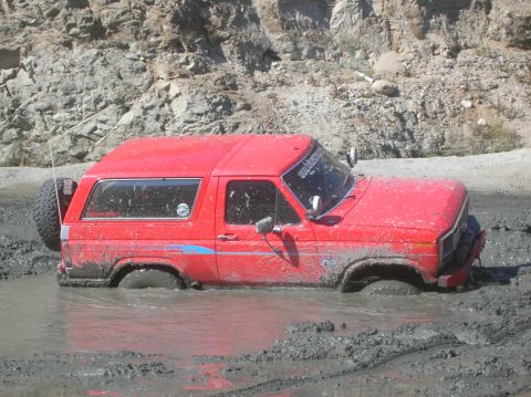 1985 Ford Bronco - This red Ford Bronco is stuck deep in a mud pit, with only the roof and upper body visible above the muck.
