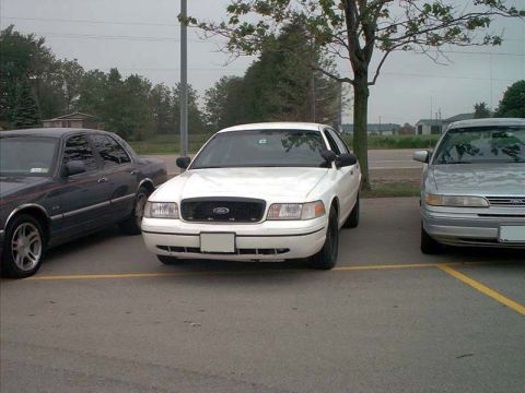 2000 Ford Crown Victoria - A white 2000 Ford Crown Victoria is parked in a lot, flanked by two other sedans.