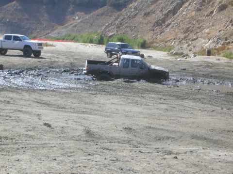 1985 Ford Bronco - A truck is stuck in a muddy area with other vehicles in the background.