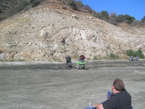 1985 Ford Bronco - Several ATVs are being ridden on a dirt track with a rocky hillside in the background.