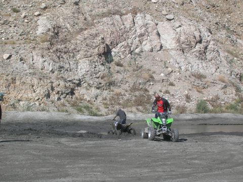 1985 Ford Bronco - A green ATV tows a stuck ATV through a muddy, rocky terrain.