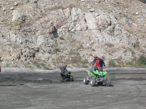 1985 Ford Bronco - Two ATVs are being ridden on a dirt track with a rocky hill in the background.