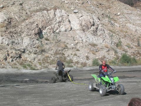 1985 Ford Bronco - One ATV tows another out of the mud in a rocky, outdoor area.