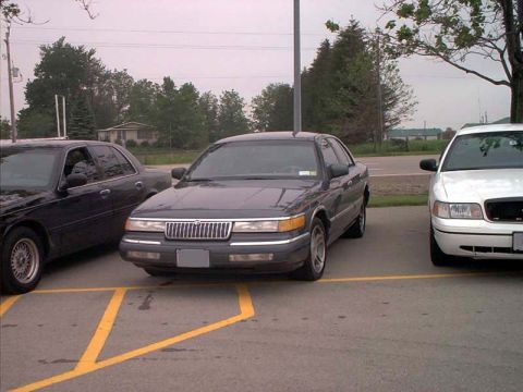 2000 Ford Crown Victoria - Two sedans, a Mercury Grand Marquis and a Ford Crown Victoria, parked in a lot.