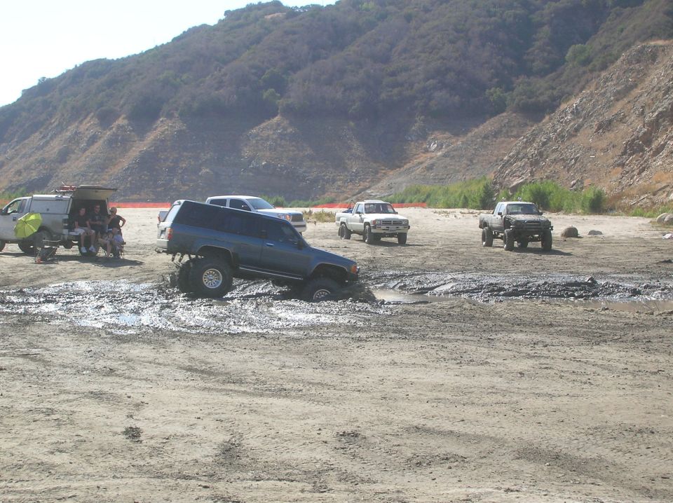 Blue SUV with lifted suspension stuck in mud, other trucks nearby