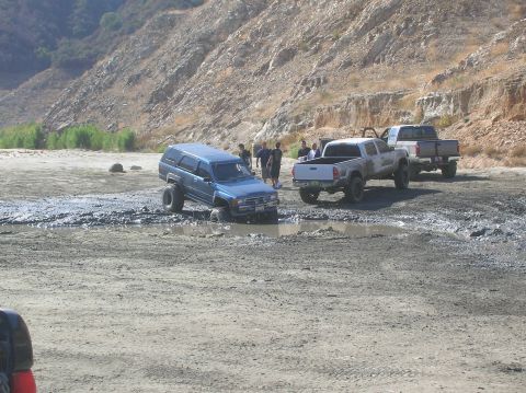1985 Ford Bronco - Several vehicles are stuck in mud with people observing the scene.
