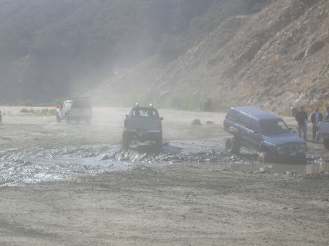 1985 Ford Bronco - Multiple 4x4 vehicles navigate a challenging muddy terrain under hazy conditions.