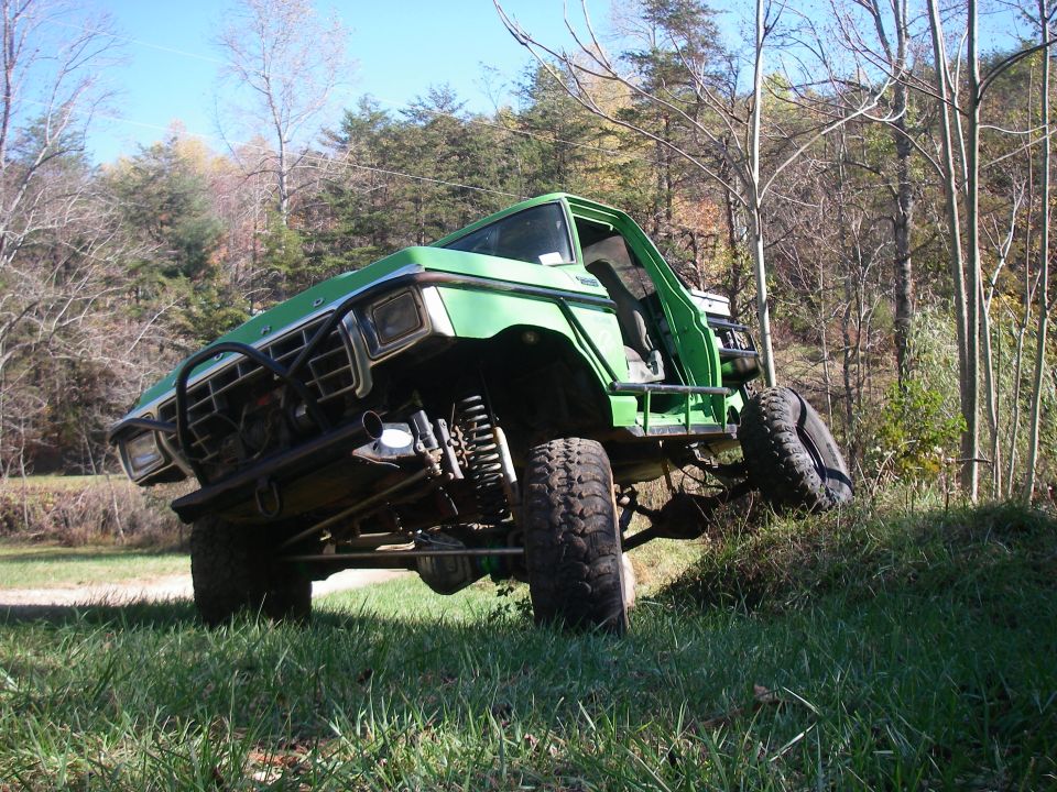 Green lifted Ford pickup with exposed suspension climbing a grassy slope