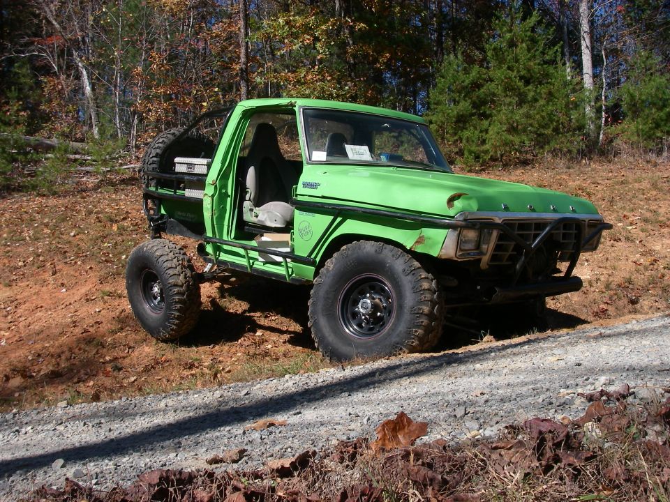 Green doorless Ford pickup parked on a dirt embankment in the woods