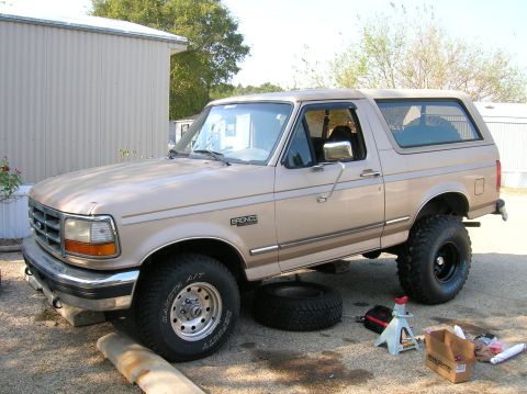 1996 Ford Bronco - Tan 1996 Ford Bronco lifted on jack stands with tires removed, suggesting maintenance or modification.