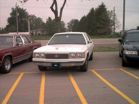 2000 Ford Crown Victoria - A white Ford Crown Victoria is parked in a lot next to other vehicles.