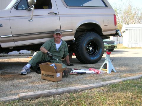 1996 Ford Bronco - A man works on a lifted Ford Bronco, surrounded by tools and a Rough Country suspension box.