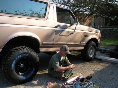 1996 Ford Bronco - A man works on a lifted Ford Bronco, surrounded by tools and parts.