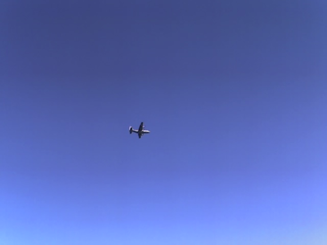Airplane flying in a clear blue sky. Supermotors.net logo in lower right