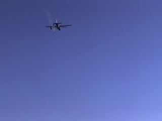 1988 Ford Bronco - An airplane is captured in mid-flight against a vast expanse of blue sky, with a website logo visible at the bottom.