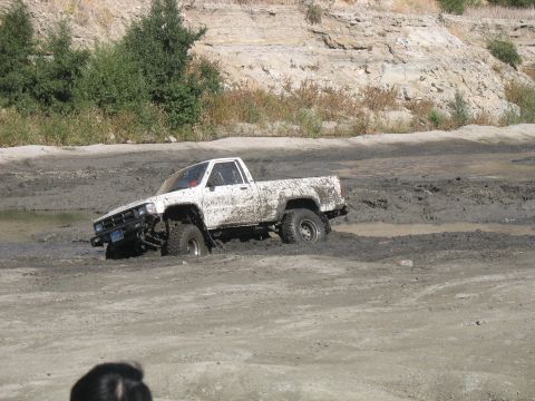 1987 Ford Bronco - A white pickup truck is stuck in a mud pit with the front left wheel deep in the mire.