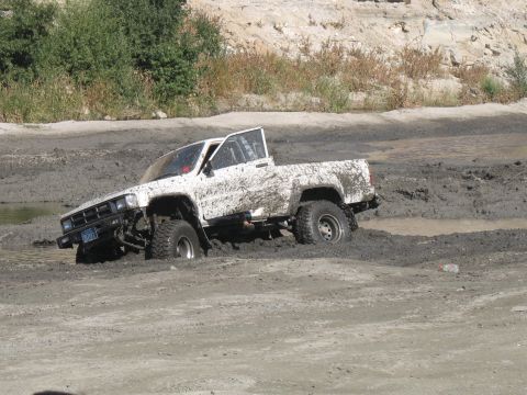 1987 Ford Bronco - This white Toyota pickup truck appears to be stuck in a muddy off-road area, with the driver's door ajar.