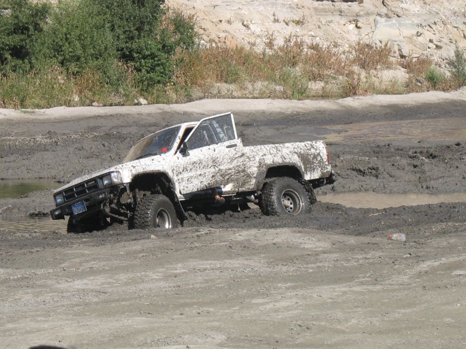 White 1984 Toyota pickup truck stuck in mud, driver's door open