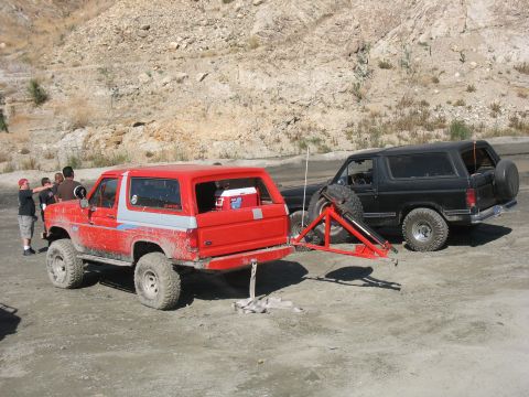 1987 Ford Bronco - Red 1987 Ford Bronco towing a black Ford Bronco with a dolly in a dirt area.