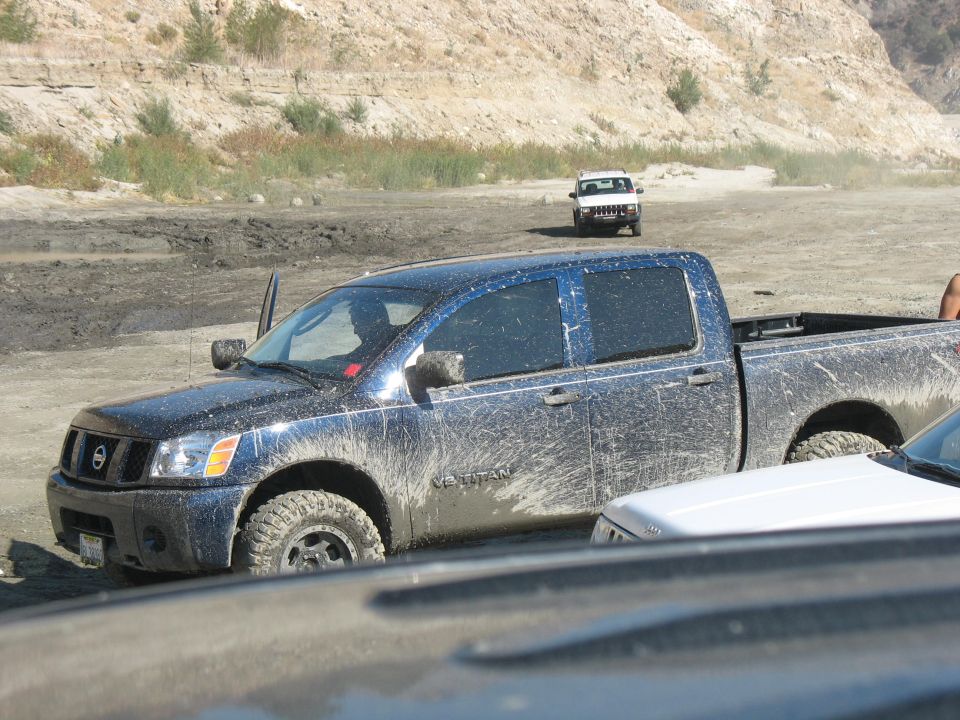 Muddy blue Nissan Titan pickup truck with door open, another white SUV in background