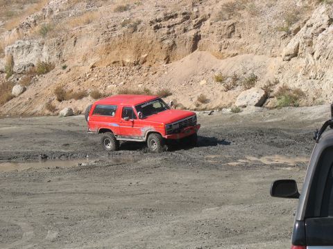 1987 Ford Bronco - Red 1987 Ford Bronco navigating a muddy off-road trail, with another vehicle nearby.