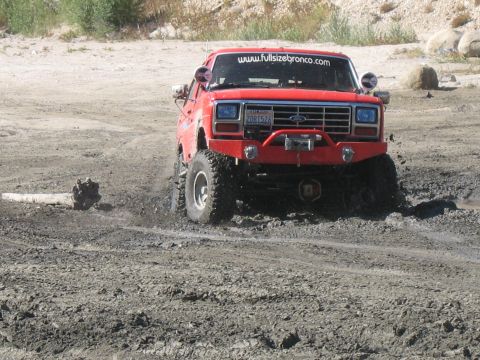 1987 Ford Bronco - This red 1987 Ford Bronco navigates a muddy off-road course, displaying a winch and custom bumper.